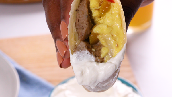 A hand holding half of a breakfast burrito that was dipped in a white sauce