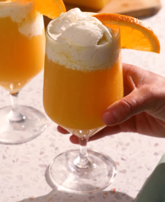 a hand holding a mimosa float in a wine glass