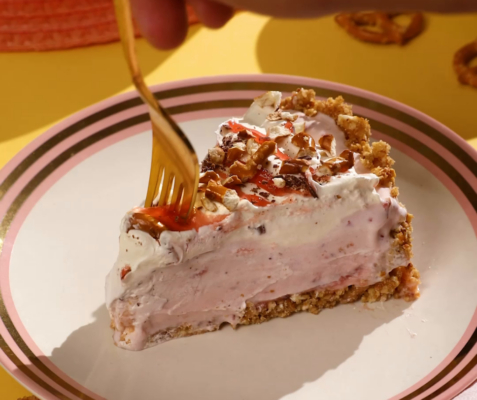 a fork cutting into a slice of strawberry pretzel ice cream pie on a plate