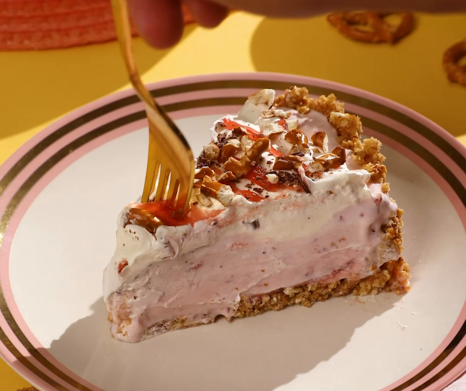 a fork cutting into a slice of strawberry pretzel ice cream pie on a plate