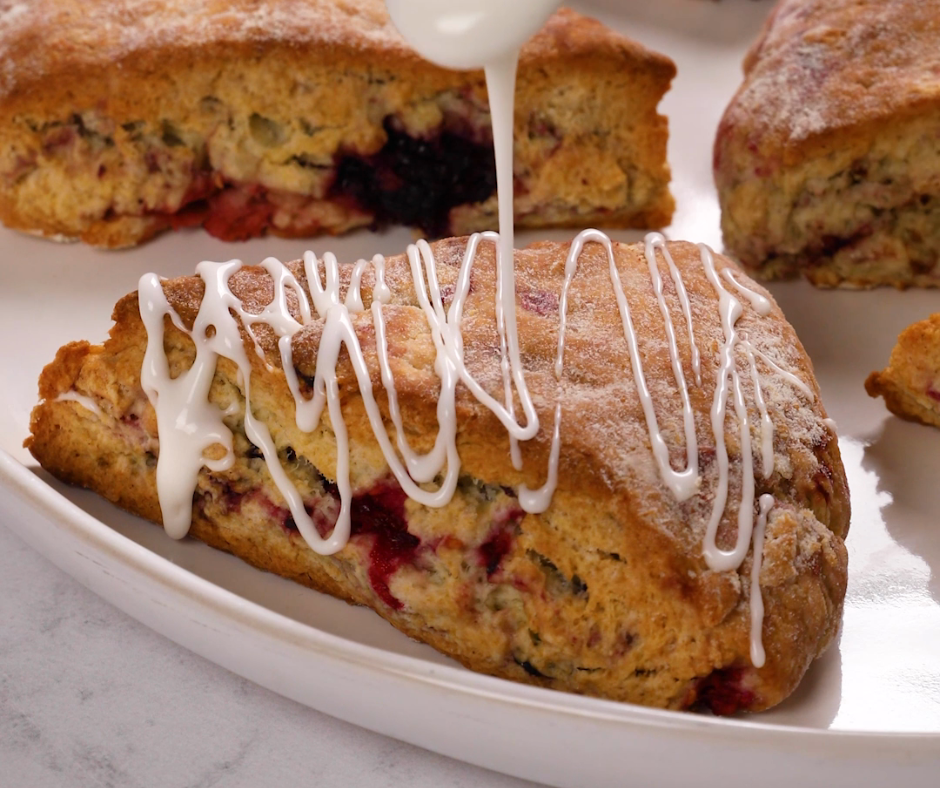 a triple berry vanilla scone being drizzled with icing