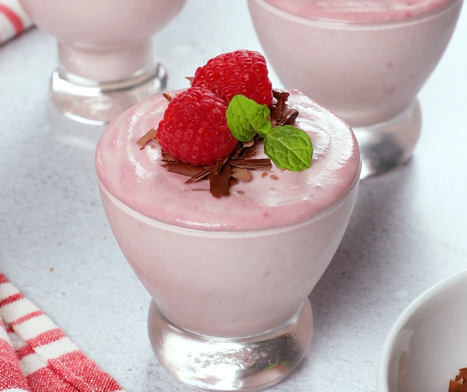 a small bowl filled with raspberry ricotta mousse topped with chocolate shreds, raspberry, and mint