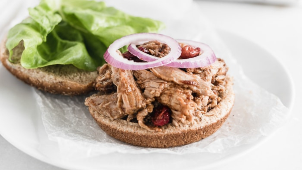 two pieces of bread, one wit pulled pork and onions on top and the other topped with lettuce